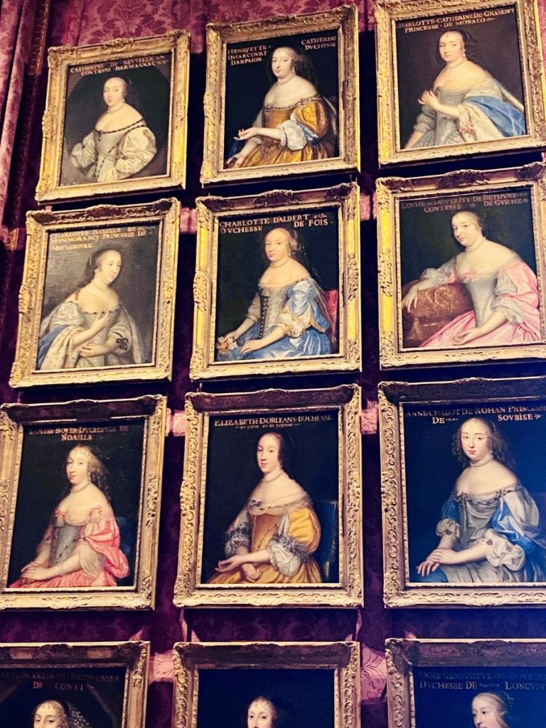 Portraits of French nobility and royalty hanging in the Palace of Versailles — timeless artwork that helps answer: is Versailles worth visiting?