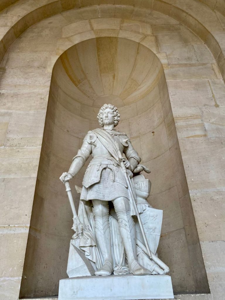Marble statue of a male figure in the Hall of Mirrors, surrounded by reflective walls, gilded decor, and opulent historical detail.